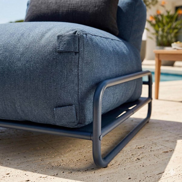 Nahaufnahme eines Outdoor-Sessels mit blauem Polster aus Webstoff und einem Gestell aus dunkelblauem Metall auf einer Terrasse.