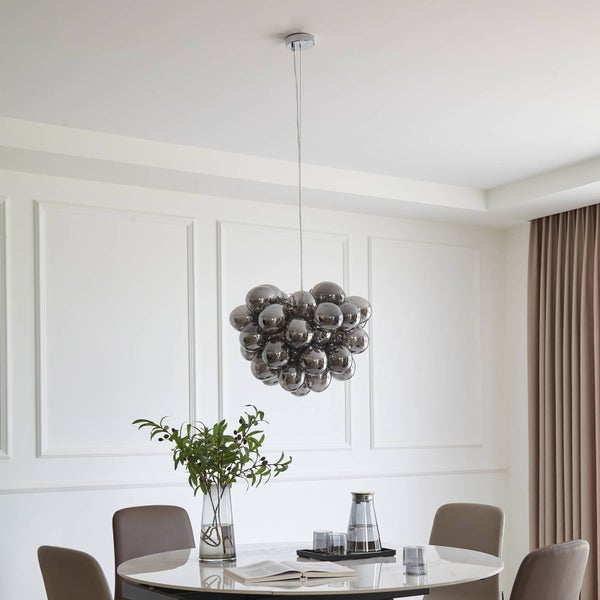 Moderne Pendelleuchte mit rauchgrauen Glaskugeln über einem runden Marmortisch in einem hellen, organisierten Esszimmer.