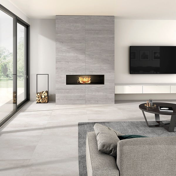 Modernes Wohnzimmer mit Kamin verkleidet in horizontal geriffelten Steinplatten und großformatigen Bodenfliesen in Betonoptik.