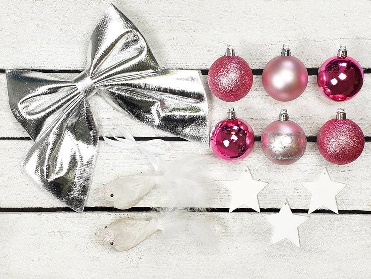 Set mit Weihnachtsbaumschmuck bestehend aus einer Schleife, Weihnachtskugeln, Vögeln mit Federn und sternförmigen Anhängern auf Holzoberfläche