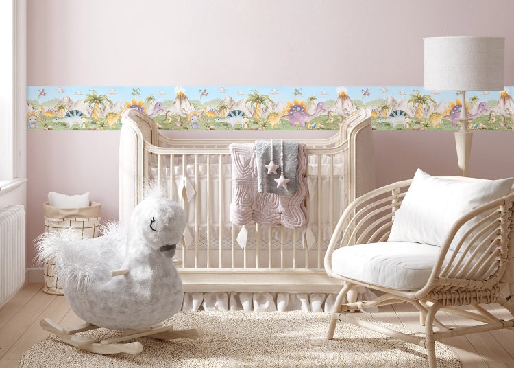 Wandbordüre mit bunten Dinosaurier-Motiven in einem hellen Kinderzimmer mit Babybett, Schwanen-Schaukeltier und Rattan-Sessel.