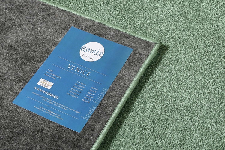 Grüner getufteter Teppich Venice aus 100 Prozent Polypropylen mit homie LIVING Logo, Pflegehinweisen und OEKO-TEX Standard 100 Zertifizierung.