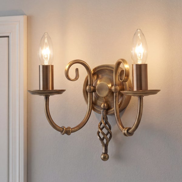 Klassische, zweiflammige Wandleuchte aus Messing mit eingeschalteten Kerzenlampen, montiert an einer Wand.