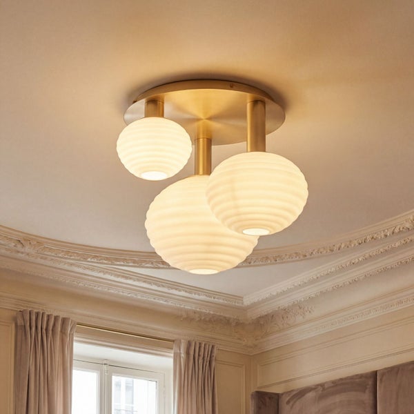 Dreiflammige Deckenleuchte mit geriffelten Glaskugeln und Messinghalterung in einem klassisch gestalteten, hellen Raum mit Stuckverzierungen.