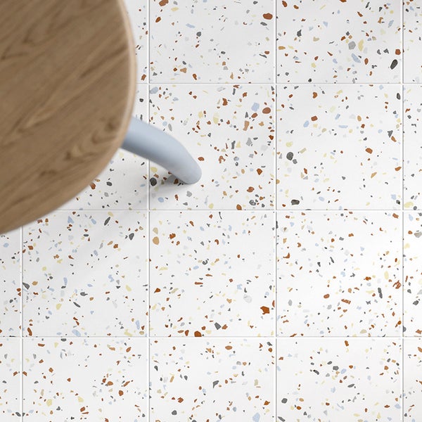 Quadratische Bodenfliesen mit Terrazzo Optik in einer modernen Inneneinrichtung mit einem Holzstuhl.