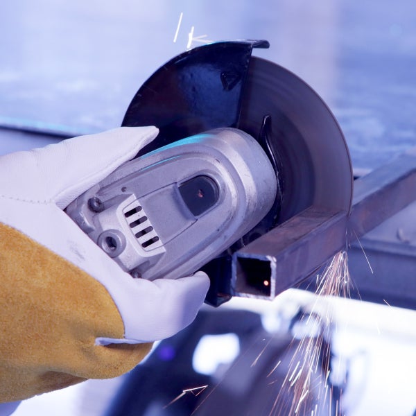 Winkelschleifer schneidet ein Metallprofil mit Funkenflug, Hand in einem Schutzhandschuh.