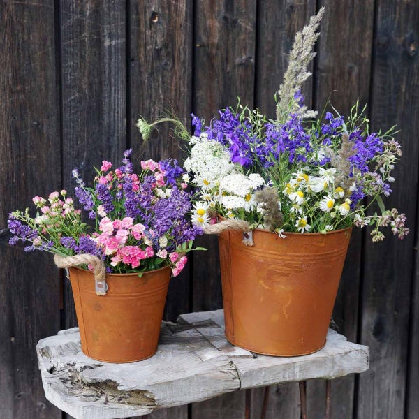 Zwei Zinkeimer mit bunten Blumensträußen auf einem Holztisch vor einer Holzwand