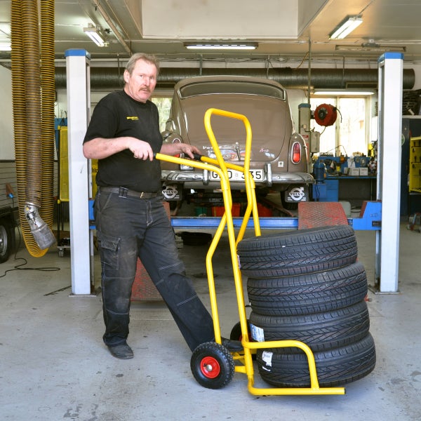 Mann schiebt Reifentransportwagen mit Reifen in Werkstatt