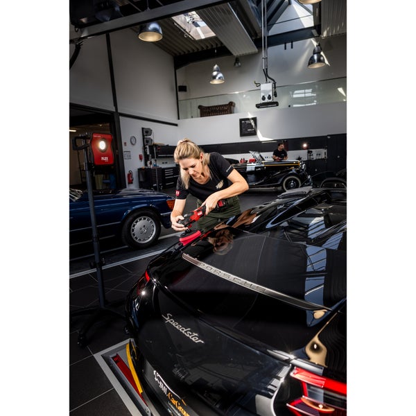 Eine Person poliert mit einer Akku Poliermaschine von FLEX die Karosserie eines schwarzen Porsche in einer professionellen Werkstatt.