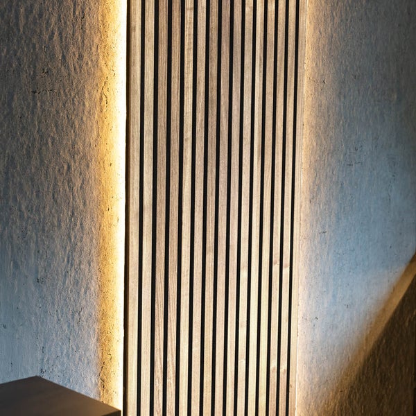 Akustikpaneel aus Holzlamellen an einer strukturierten Wand mit LED Beleuchtung.