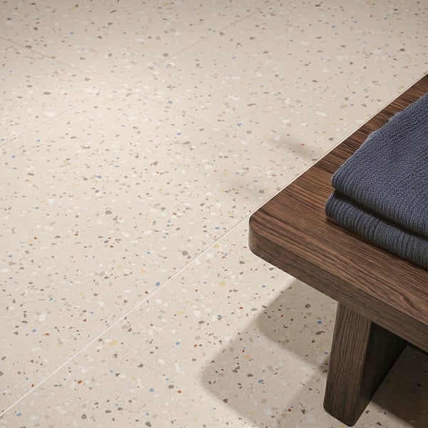 Fliesen mit Terrazzo Optik verlegt auf einem Boden mit einem Teil eines hölzernen Möbelstücks und Textilien im Vordergrund.