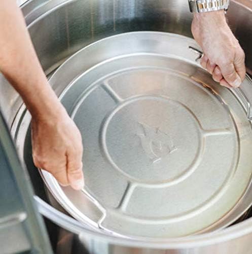 Person setzt eine runde Metallschale mit Flammen-Symbol in einen Grill oder eine Feuerschale ein.