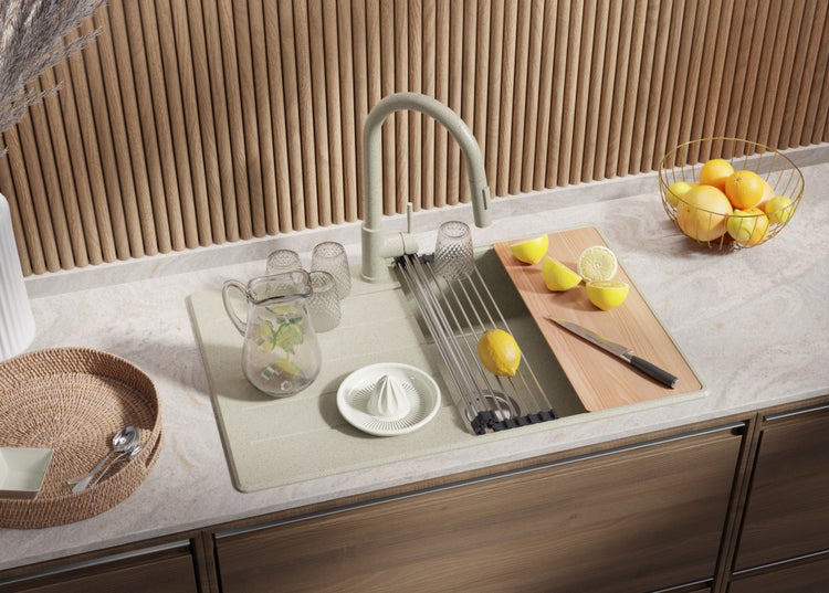 Küchenspüle mit Armatur, Abtropfgestell, Schneidebrett, Zitronenpresse und Gläsern auf einer Küchentheke.