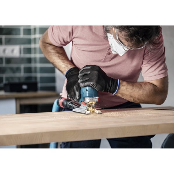 Mann arbeitet mit Stichsäge an Holzbrett, trägt Schutzbrille und Handschuhe