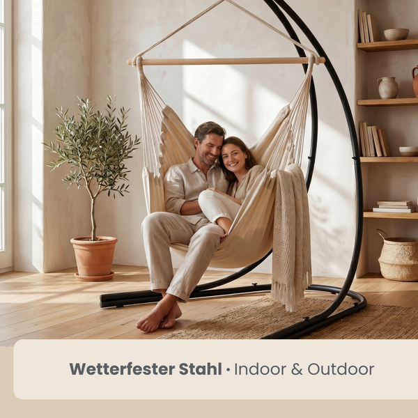 Ein Paar in einem beigen Hängesessel an einem schwarzen Gestell aus wetterfestem Stahl in einem hellen, minimalistisch eingerichteten Wohnzimmer.