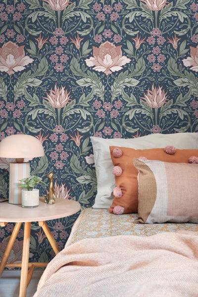 Vliestapete mit floralem Vintage-Muster in einem gemütlichen Schlafzimmer mit Bett, Beistelltisch aus Holz und einer Tischlampe.