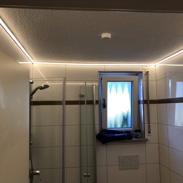Badezimmer mit Dusche, Fenster und Deckenbeleuchtung.
