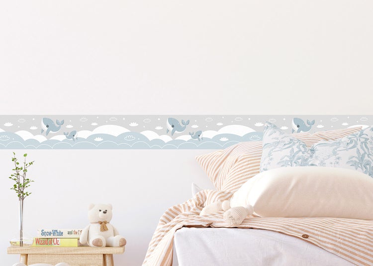 Tapetenbordüre für Kinderzimmer mit Motiven von Walen, Wolken und Sternen über einem Bett in einem hell gestalteten Kinderzimmer.