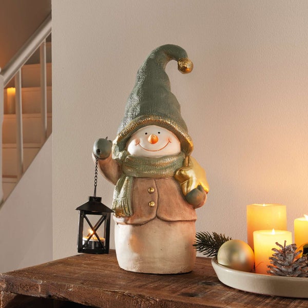 Dekorativer Schneemann mit Mütze, Laterne und Stern auf einem Tisch