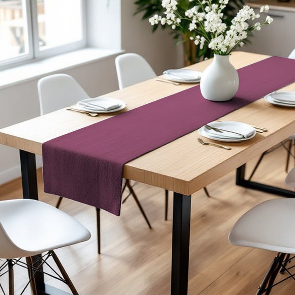 Esstisch mit burgunderrotem Tischläufer, Geschirr und Blumenvase für eine festliche Tischdekoration.