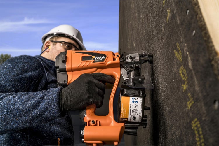 Handwerker verwendet ein Paslode Impulse Gasnagelgerät für Arbeiten an einer Holzwand im Freien.