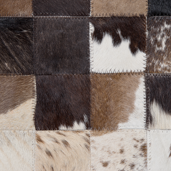 Patchwork-Teppich aus quadratischen Kuhfellstücken mit sichtbaren Zickzack-Nähten.