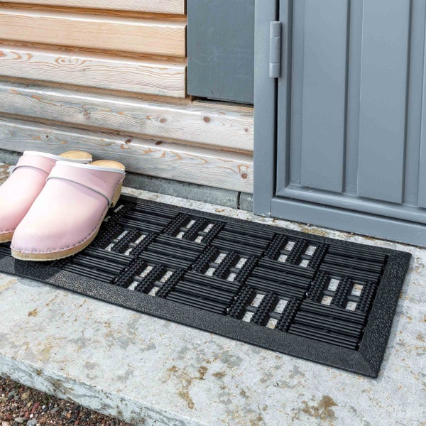 Schmutzfangmatte aus Gummi vor einer Haustür mit Holzverkleidung und Clogs.