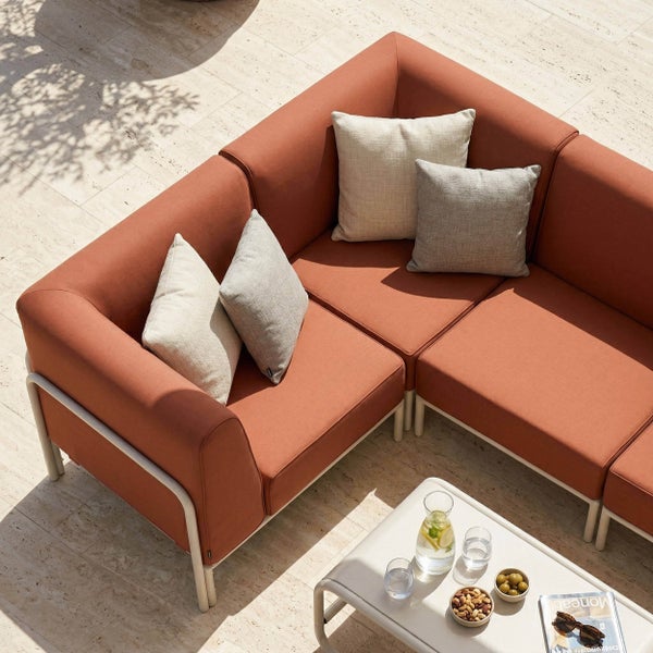 Modernes Outdoor-Lounge-Set mit rostfarbenem Ecksessel und weißem Metalltisch auf einer hellen Steinterrasse an einem Pool in sonniger Atmosphäre.