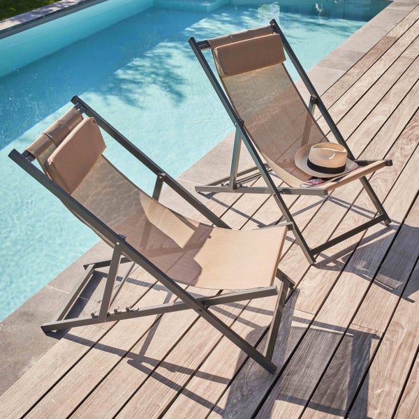 Zwei klappbare Sonnenliegen mit Kopfpolstern auf einer Holzterrasse am Pool. Metallrahmen mit Textilbespannung.