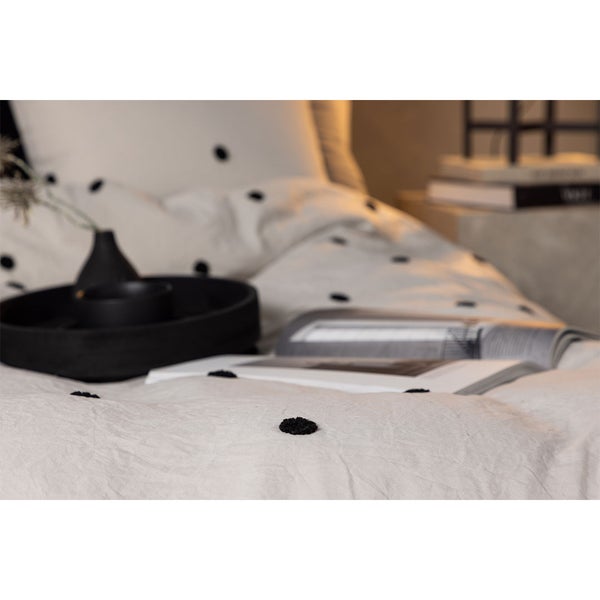 Bettwäsche mit getupftem Muster auf einem Bett mit Tablett, Vase und Zeitschriften in einer hellen und organisierten Umgebung.