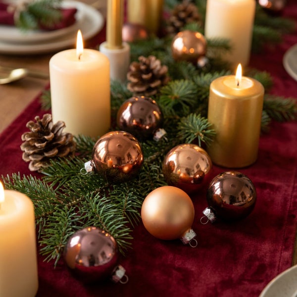 Festliche Tischdekoration mit Tannenzweigen, Weihnachtskugeln in verschiedenen Ausführungen, Tannenzapfen und brennenden Stumpenkerzen.