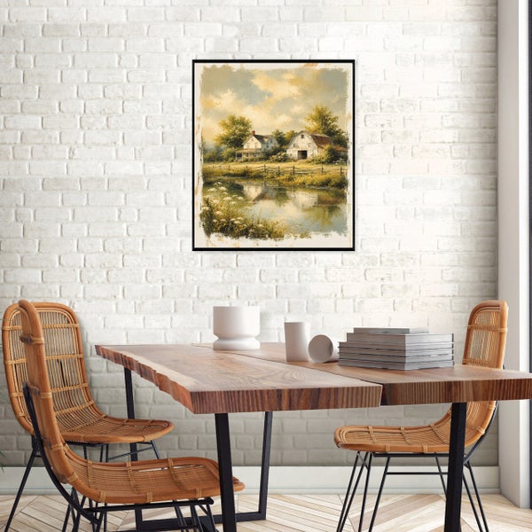 Gerahmtes Wandbild mit Landhausmotiv über einem Holztisch mit Korbstühlen vor einer weißen Backsteinwand.