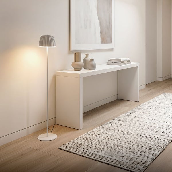Moderne, beleuchtete Stehleuchte mit Faltenlampenschirm neben einem weißen Konsolentisch in einem hellen, minimalistischen Flur.