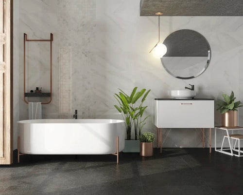 Modernes Badezimmer mit freistehender weißer Badewanne, dunklen Bodenfliesen, Wandfliesen in Marmoroptik und weißem Waschtisch mit rundem Spiegel.