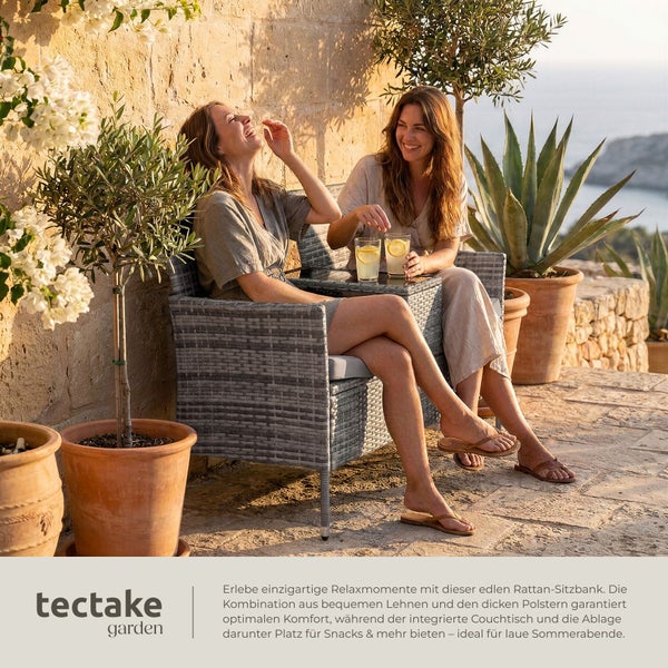 Zwei Frauen sitzen entspannt auf einer Rattan-Gartenbank mit integriertem Tisch auf einer sonnigen Terrasse.