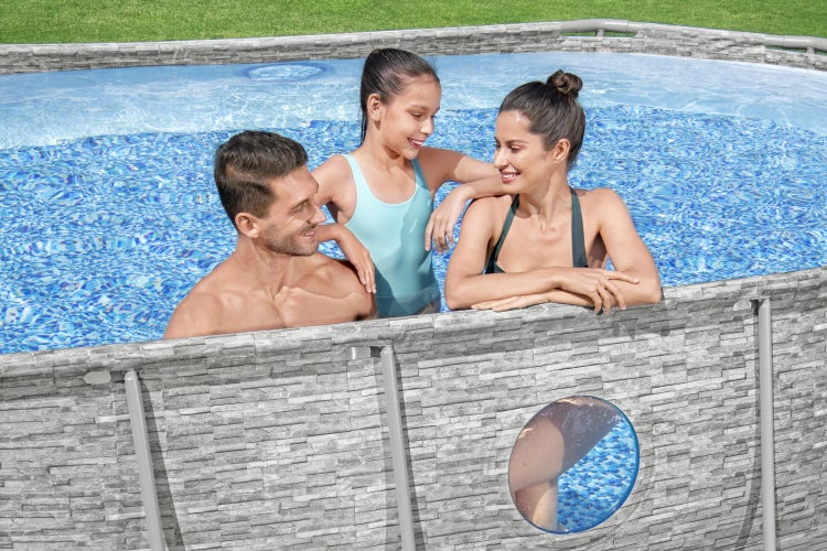 Ovaler Aufstellpool in Steinoptik mit Sichtfenster und einer Familie im Wasser.