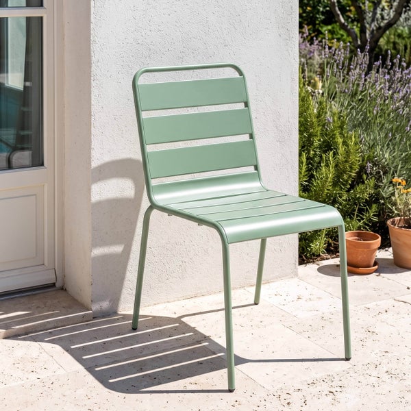 Grüner Gartenstuhl aus Metall mit Querstreben auf einer hellen Terrasse neben einer Hauswand.