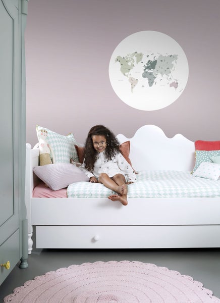 Kinderzimmer mit weißem Bett, rundem Teppich und Wandtattoo Weltkarte