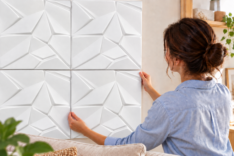 Eine Frau bringt quadratische Wandpaneele mit geometrischem Reliefmuster an einer Innenwand an, um die Wandgestaltung zu akzentuieren.