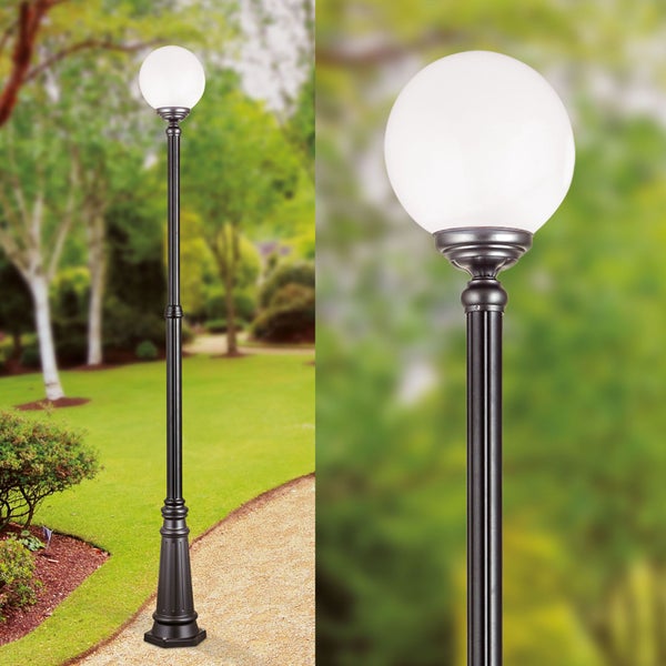 Klassische Gartenleuchte mit schwarzem Metallmast und weißem Kugelschirm, platziert neben einem Gartenweg in einer grünen Außenanlage.