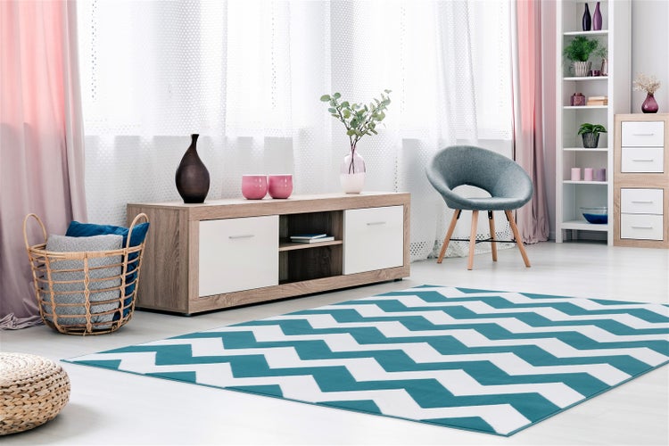 Helles Wohnzimmer mit TV-Board, grauem Sessel und einem gemusterten Teppich mit Zickzackmuster auf dem Boden.