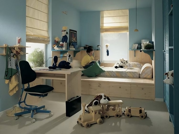 Hell gestaltetes Kinderzimmer mit Massivholzmöbeln, Schreibtisch, Funktionsbett mit Schubladen und Raffrollos vor den Fenstern.