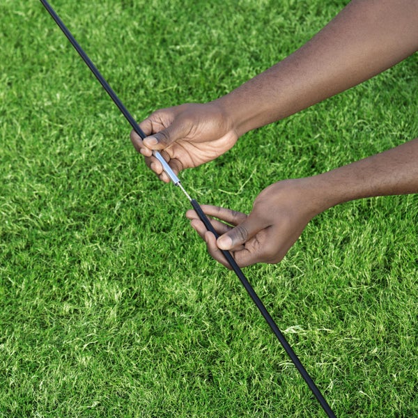 Eine Person montiert ein Zeltgestänge über einer grünen Wiese.
