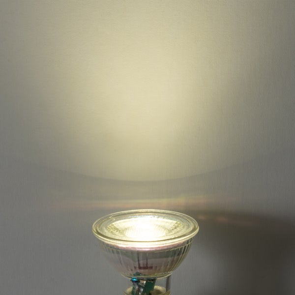 Eingeschaltete GU10 LED-Reflektorlampe mit warmweißem Lichtkegel an einer Wand.