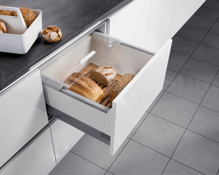 Geöffnete Küchenschublade mit Brotaufbewahrung aus Holz und transparenter Abdeckung, gefüllt mit verschiedenen Broten in einer modernen Küche.