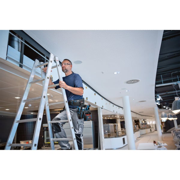 Mann mit Werkzeuggürtel auf einer Aluminiumleiter in einem Innenraum