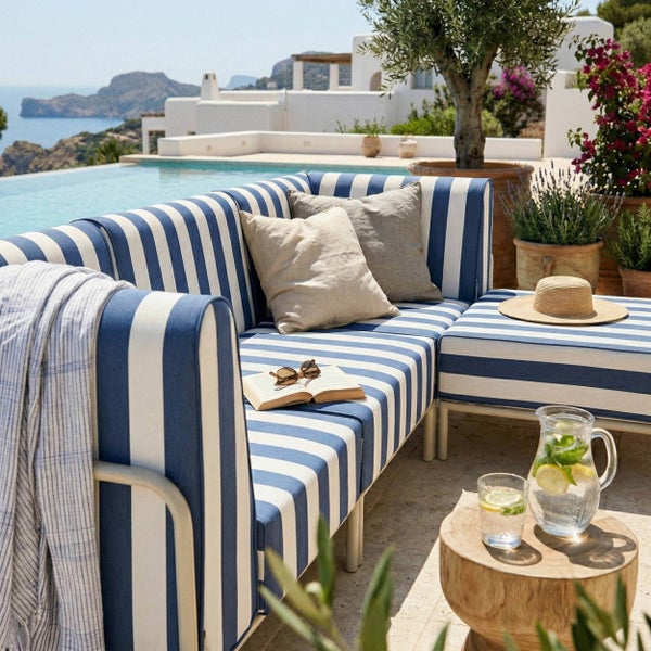 Moderne Gartenlounge mit blau-weiß gestreiften Polstern auf einer hellen Terrasse am Meer, mit hölzernem Beistelltisch und Pflanzen.