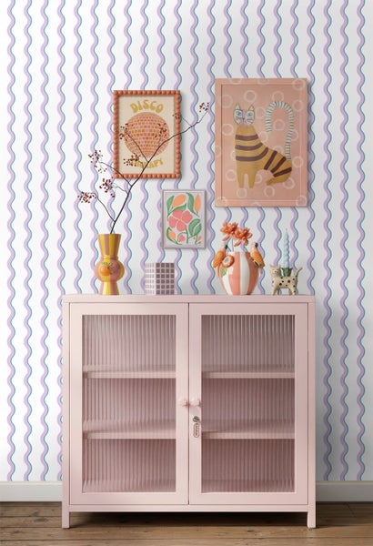 Vliestapete mit gewelltem Muster in Lila und Türkis in einem hellen Raum mit einer rosa Vitrine und bunter Dekoration.