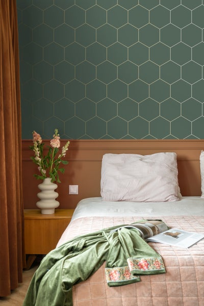 Schlafzimmer mit Bett, Nachttisch, Blumenvase und Tapete mit sechseckigem Muster