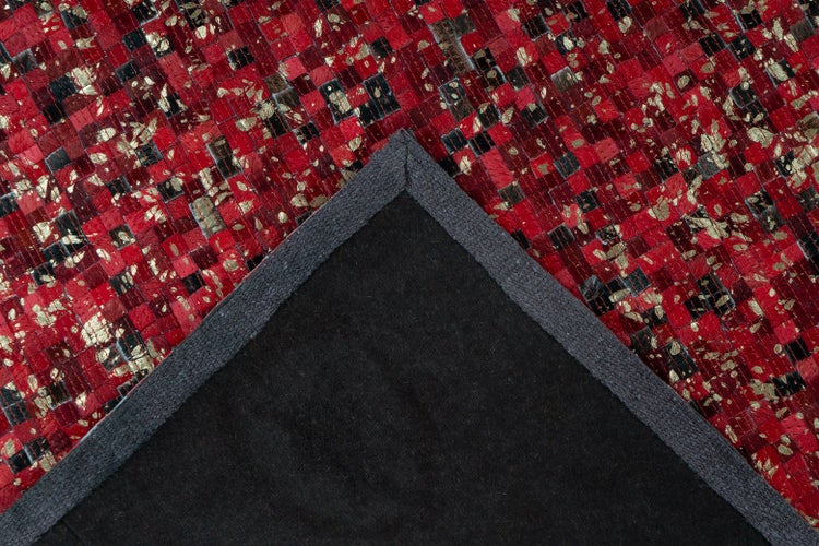 Nahaufnahme eines Lederteppichs in Rot und Gold mit dunkler Rückseite und grauer Einfassung.